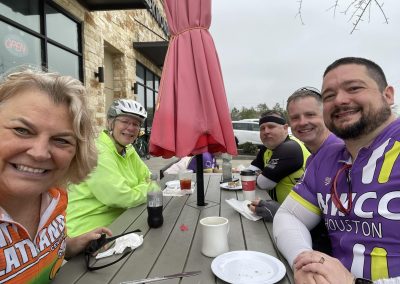 Smiling cyclists taking a break at a cafe outdoor patio during Northwest Cycling Club ride.