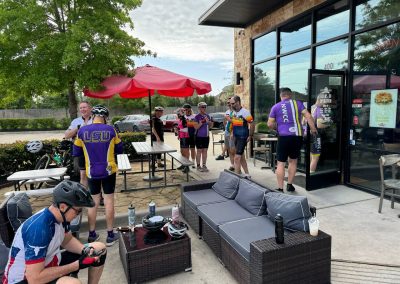 Cycling group at Northwest Cycling Club event outside coffee shop, wearing cycling gear and helmets.