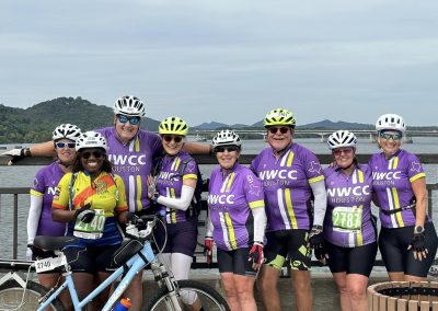Group of cyclists wearing NWCC Houston jerseys posing together on a bridge for a cycling event.