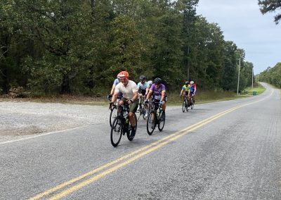 Group of cyclists riding on a scenic country road with lush greenery in the background.