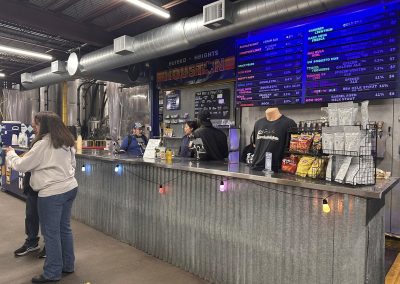 Cycling In Houston - NWCC Recent Activities Gallery 643 Brightly lit indoor brewery bar at Northwest Cycling Club with digital beer menu display.