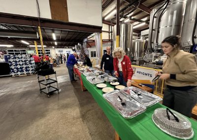 Cycling In Houston - NWCC Recent Activities Gallery 613 Indoor brewery event with people serving food and drinks at Northwest Cycling Club gathering, festive holiday atmosphere.
