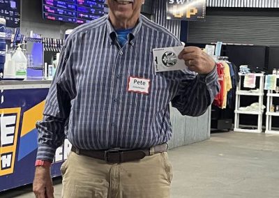 Cycling In Houston - NWCC Recent Activities Gallery 654 Older man smiling at cycling event, holding a ticket, in an indoor sports venue.