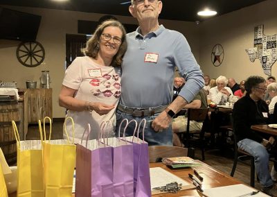 Cycling In Houston - NWCC Recent Activities Gallery 552 Elderly couple smiling at a Northwest Cycling Club event with gift bags on the table.