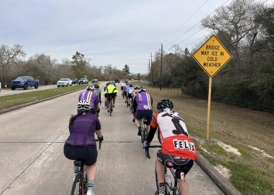 Cycling In Houston - NWCC Recent Activities Gallery 544 Cyclists riding on a road in Northwest Cycling Club, with a warning sign about icy weather on the bridge.