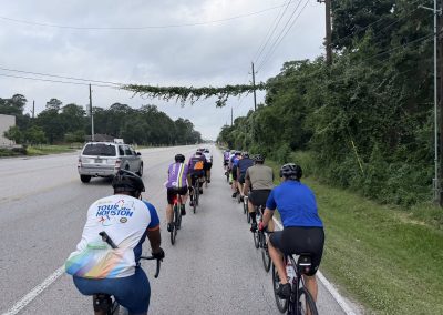 Cycling In Houston - NWCC Recent Activities Gallery 511 Group of cyclists riding on a scenic road with greenery and utility poles, promoting outdoor fitness and cycling community.