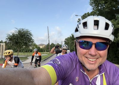 Cycling In Houston - NWCC Recent Activities Gallery 502 Smiling cyclist taking a selfie during a group ride with fellow bikers on a scenic suburban road.