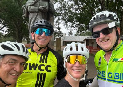 Cycling In Houston - NWCC Recent Activities Gallery 487 Smiling cyclists in NWCC gear enjoying a ride outdoors with trees and a statue in the background.