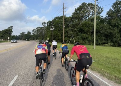 Cycling In Houston - NWCC Recent Activities Gallery 493 Brightly colored cyclists riding on a scenic road with trees in the background, promoting Northwest Cycling Club and outdoor cycling events.