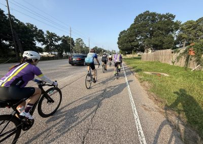 Cycling In Houston - NWCC Recent Activities Gallery 477 Cycling group riding on a scenic road with lush trees and clear sky, promoting Northwest Cycling Club outdoor biking adventures.