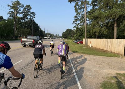 Cycling In Houston - NWCC Recent Activities Gallery 480 Cycling group riding on a scenic road with trees, cars, and fellow cyclists, part of Northwest Cycling Club.