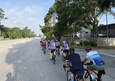 Cycling In Houston - NWCC Recent Activities Gallery 466 Cycling group riding on a suburban road with trees and houses, members wearing NWCC apparel for Northwest Cycling Club.