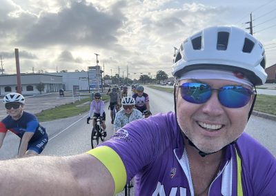 Cycling In Houston - NWCC Recent Activities Gallery 464 Smiling cyclist wearing purple jersey and sunglasses taking group ride on open road.
