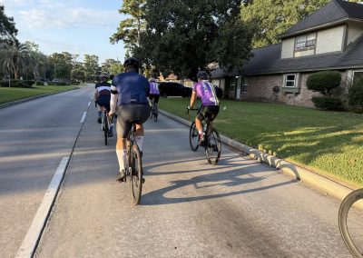 Cycling In Houston - NWCC Recent Activities Gallery 380 Group of cyclists riding on a suburban street with trees and houses, promoting Northwest Cycling Club and cycling community.