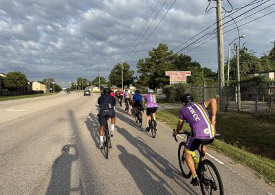 Cycling In Houston - NWCC Recent Activities Gallery 365 Group of cyclists riding on a city street with clouds in the sky, promoting Northwest Cycling Club.