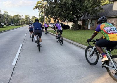 Cycling In Houston - NWCC Recent Activities Gallery 379 Group of cyclists riding on residential street with lush greenery, promoting Northwest Cycling Club.
