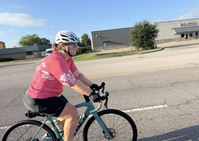Cycling In Houston - NWCC Recent Activities Gallery 341 Vegan woman cycling on the road in a pink shirt, participating in Northwest Cycling Club event.