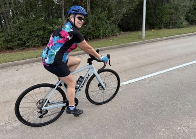 Cycling In Houston - NWCC Recent Activities Gallery 324 Bright woman cycling on road in NW cycling club gear, enjoying outdoor biking adventure.