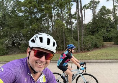Cycling In Houston - NWCC Recent Activities Gallery 321 Smiling cyclist wearing purple jersey and white helmet on scenic road with lush trees in Northwest Cycling Club.
