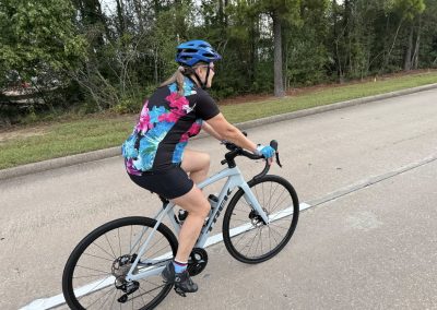 Cycling In Houston - NWCC Recent Activities Gallery 322 Woman riding a Trek road bike with helmet and cycling gear on paved trail in greenery.