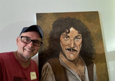 Cycling In Houston - NWCC Recent Activities Gallery 246 Portrait of a smiling man with a mustache next to a painting of Albert Einstein.