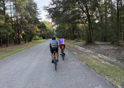 Cycling In Houston - NWCC Recent Activities Gallery 221 Two cyclists riding on a scenic wooded trail with Northwest Cycling Club branding, promoting outdoor biking.