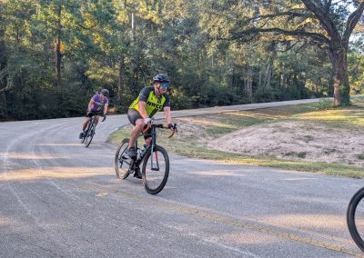 Cycling In Houston - NWCC Recent Activities Gallery 211 Cycling group riding on scenic country road with trees and sunlight, Northwest Cycling Club outdoor cycling event.