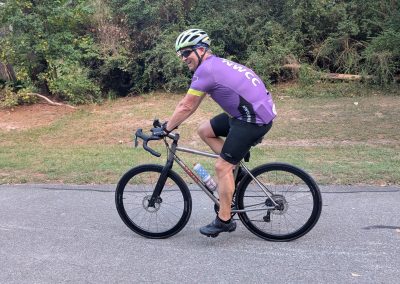 Cycling In Houston - NWCC Recent Activities Gallery 193 Man riding a bike in a cycling club jersey on a paved trail with greenery in the background.