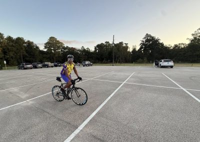 Cycling In Houston - NWCC Recent Activities Gallery 236 Cyclist in Northwest Cycling Club gear riding bike in empty parking lot at sunset.