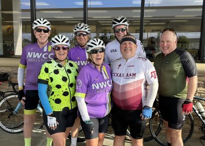 Cycling In Houston - NWCC Recent Activities Gallery 126 Group of cyclists in colorful jerseys outside a bike shop, representing Northwest Cycling Club Houston.