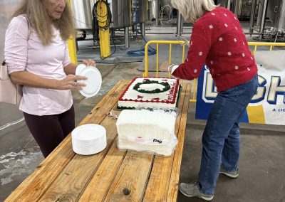 Cycling In Houston - NWCC Recent Activities Gallery 73 Celebrating Northwest Cycling Club with cake in a brewery setting and brewing equipment in the background.