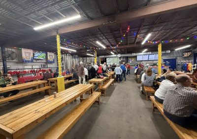 Cycling In Houston - NWCC Recent Activities Gallery 82 Indoor brewery event space with communal picnic tables, colorful string lights, and a lively atmosphere for Northwest Cycling Club members.
