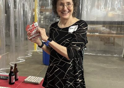 Cycling In Houston - NWCC Recent Activities Gallery 53 Smiling woman at Northwest Cycling Club event holding a wrapped gift, indoor celebration, casual cycling community gathering.
