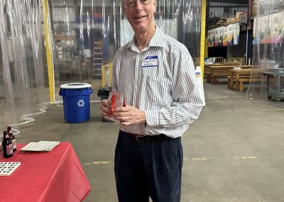 Cycling In Houston - NWCC Recent Activities Gallery 44 Happy senior man at Northwest Cycling Club event, holding a small gift, in an indoor setting with transparent plastic curtains.