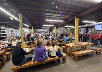 Cycling In Houston - NWCC Recent Activities Gallery 76 Bright indoor brewery tasting room with cyclists, casual seating, festive string lights, and a lively social atmosphere.