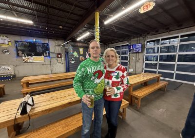 Cycling In Houston - NWCC Recent Activities Gallery 60 Festive cyclists wearing holiday sweaters at Northwest Cycling Club event, celebrating with drinks inside a brewery.
