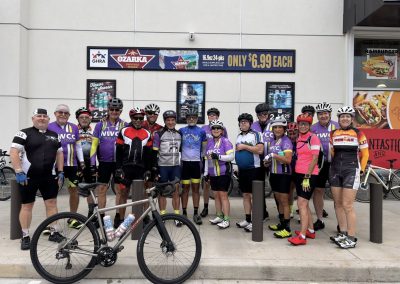 Cycling In Houston - NWCC Recent Activities Gallery 39 Large group of cyclists in colorful gear posing outside in front of a signboard.